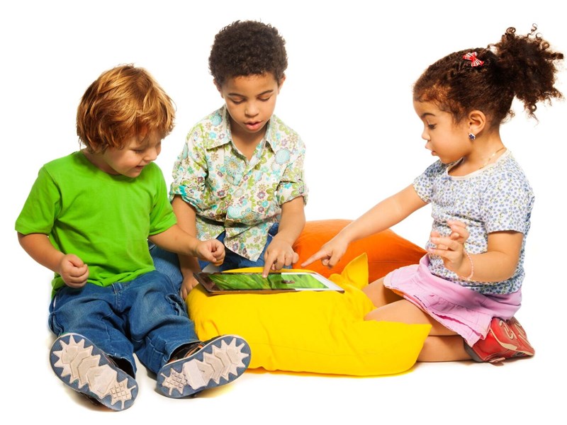 Photo image of three children sitting around a yellow beanbag and playing a game together (Shutterstock image)