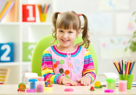 Photo image of a child playing with playdough on a table looking directly into the camera (Shutterstock image)